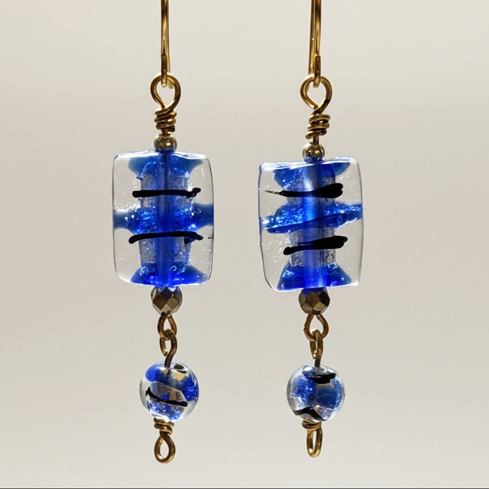Close-up of handmade cobalt blue lampwork glass drop earrings showing 13mm × 15mm rectangular bead with black brushstroke detail, faceted brass spacer, and 8mm coordinating round lampwork bead drop on custom brass fish hook wires.