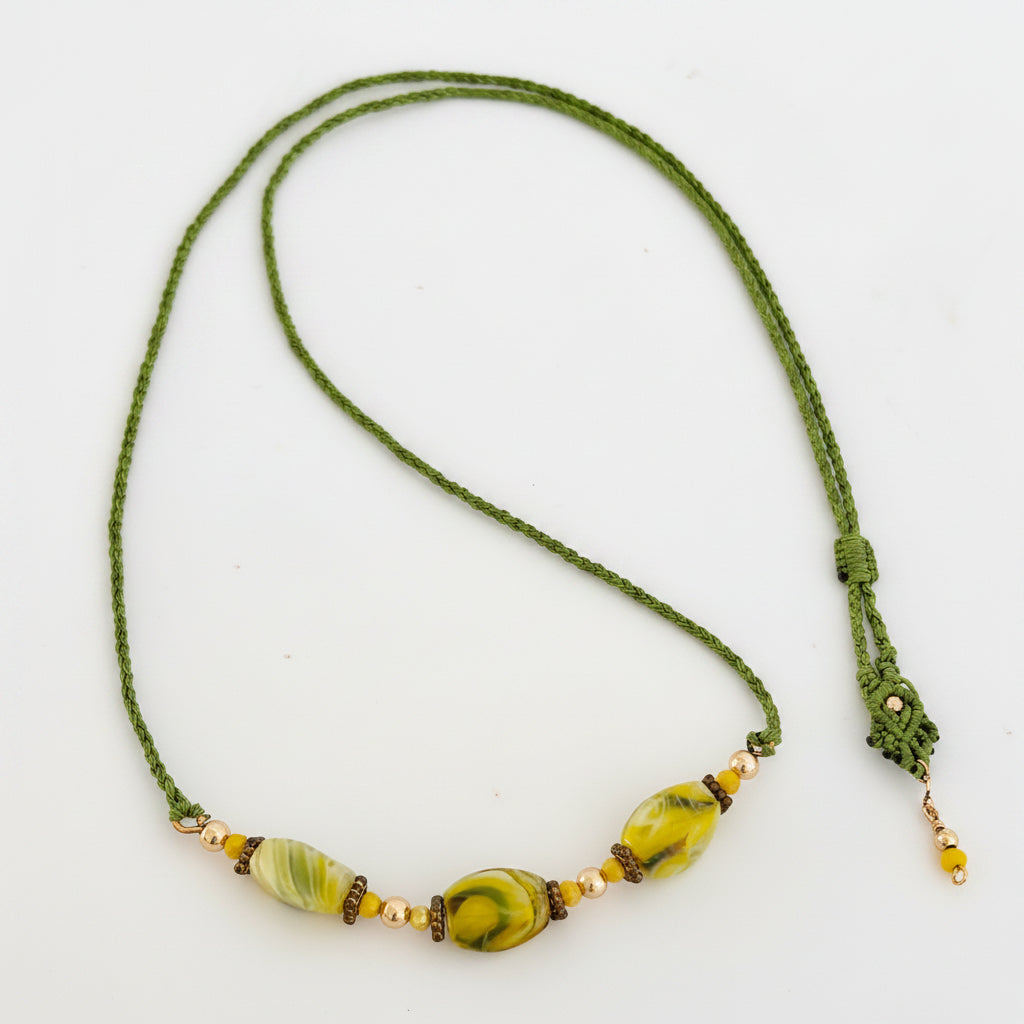 Handcrafted grass green macrame cord necklace with three twisted rectangle chartreuse lampwork glass beads (8mm × 13mm), 4mm round gold-tone beads, 3mm opaque yellow crystal accents, brass rondelle spacers, decorative slide closure, and gold-tone bead dangle, displayed on white background.