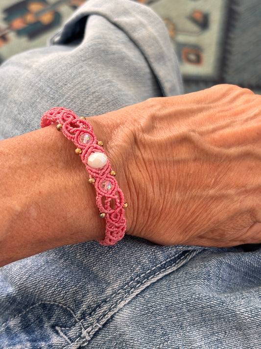 Salmon pink macrame bracelet with white rondelle and pink crystal accents worn over denim.