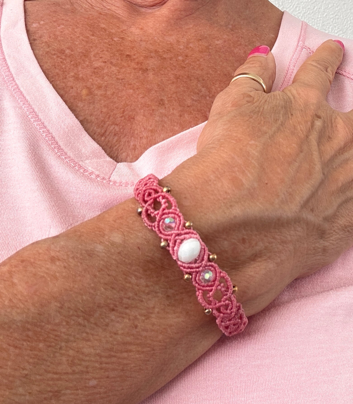 Salmon pink macrame bracelet worn with a pink top and gold ring.