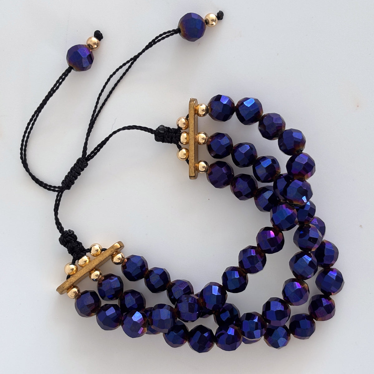Triple strand cobalt blue vitrail glass bracelet with gold-tone separators and adjustable macramé closure.