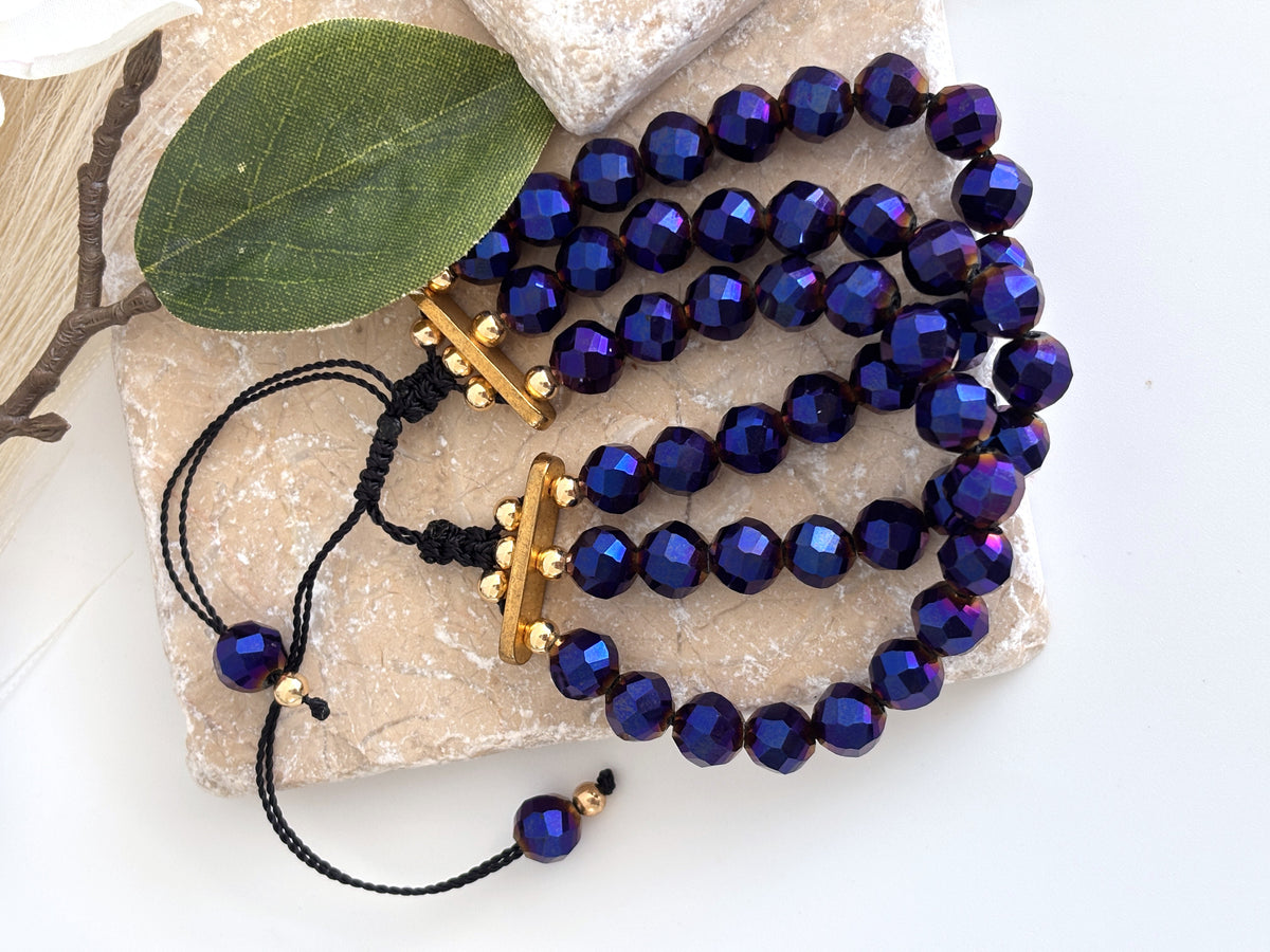Triple strand cobalt blue vitrail glass bracelet draped on travertine stone with greenery.