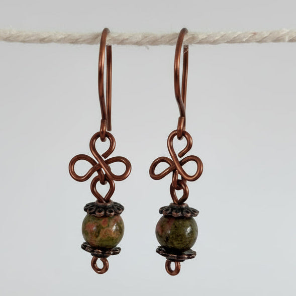 Handmade unakite gemstone drop earrings with antique copper clover charm and handcrafted copper ear wires, hanging against a neutral background.