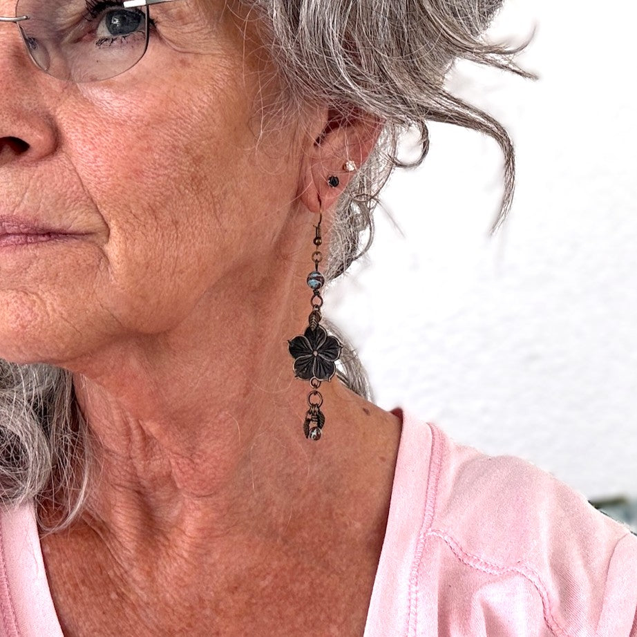 Bronze flower charm earring with calsilica bead and leaf drop shown worn on model with silver hair