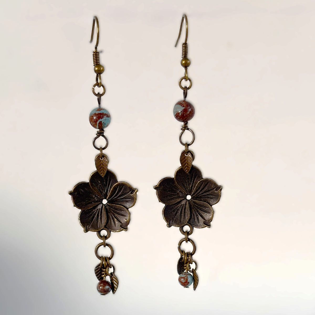 Handmade bronze flower charm earrings with calsilica beads and bronze leaf accent drops, hanging against a neutral background