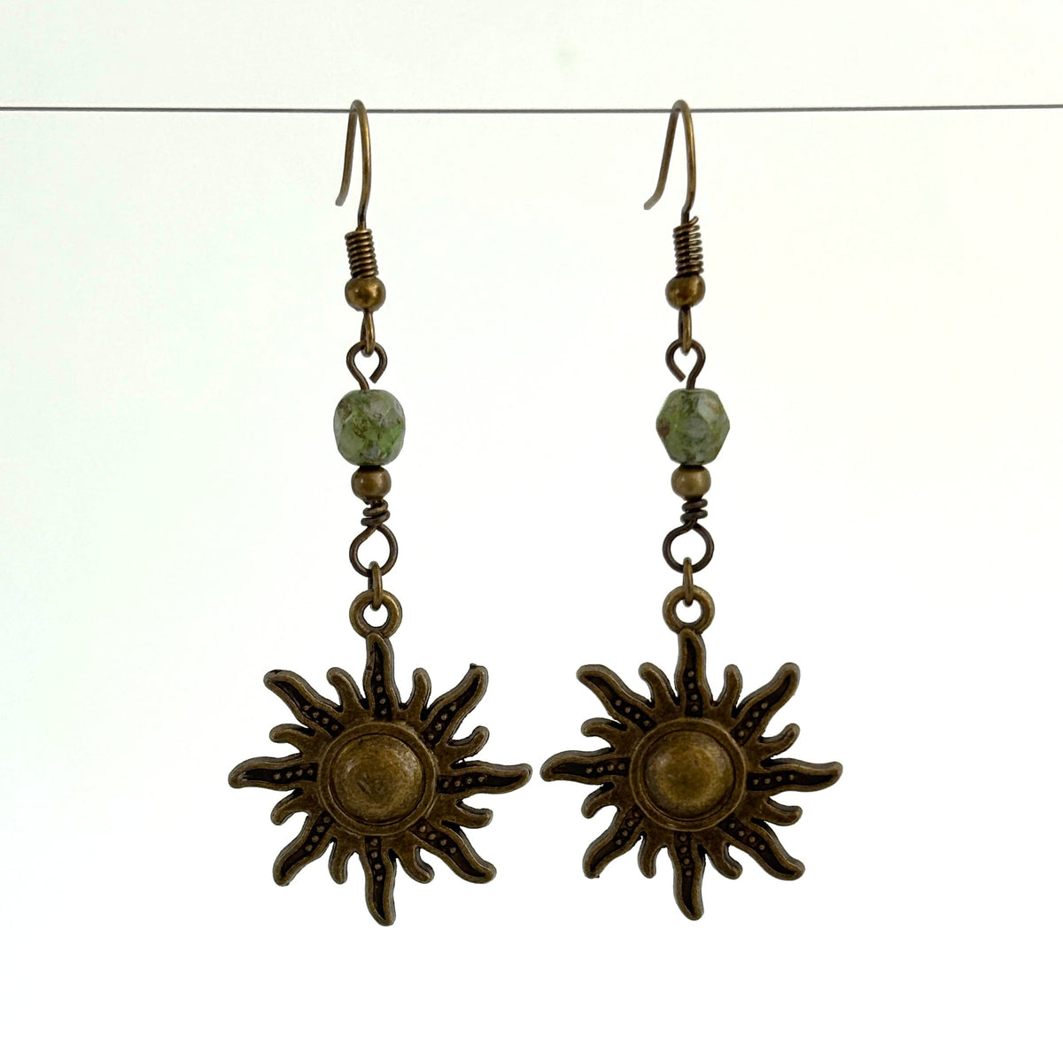 Handmade bronze sunburst charm earrings with green Picasso Czech bead and bronze accent, hanging against a neutral background