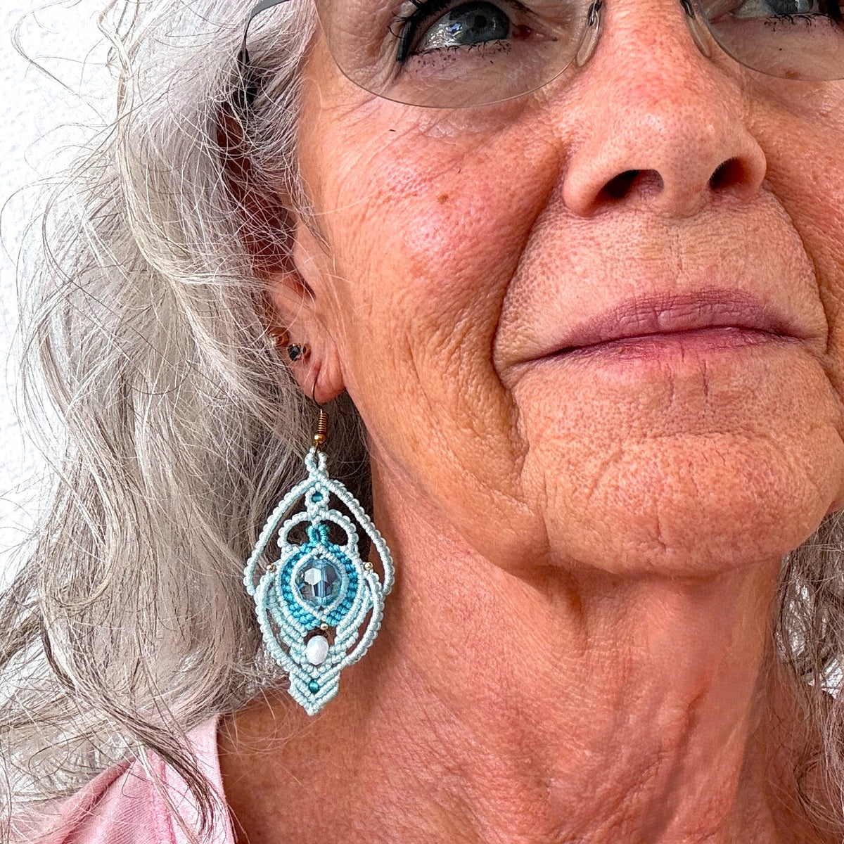 Aqua lace macrame peacock earrings with faceted glass center bead and iridescent rondelle shown worn on model with silver hair