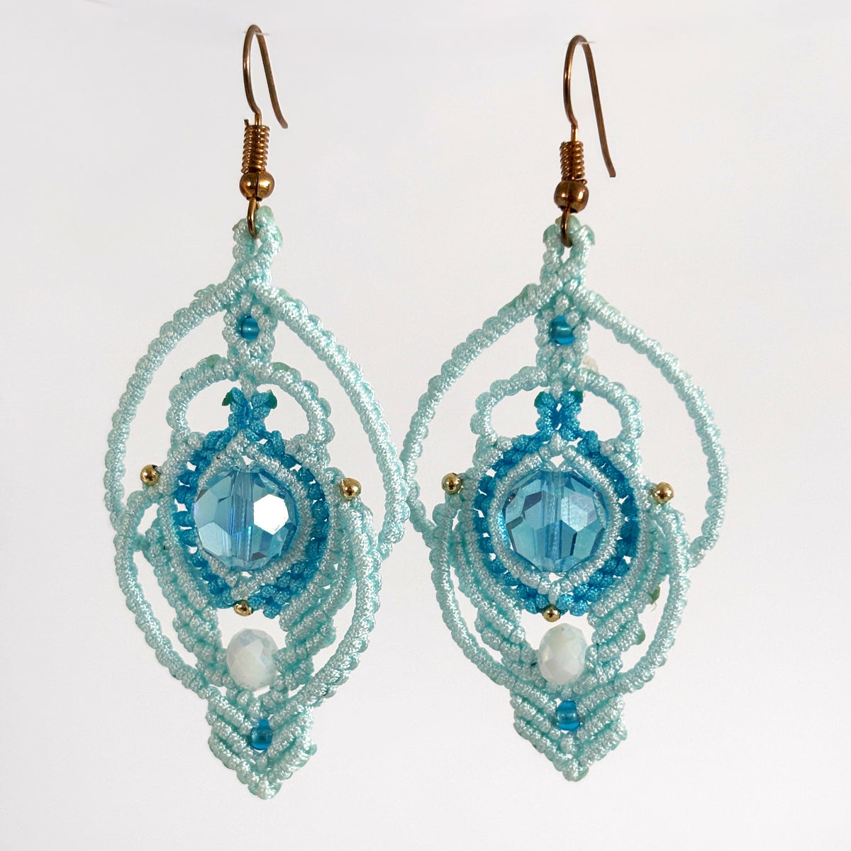 Handmade aqua two-tone lace macrame peacock earrings with faceted aqua glass bead and iridescent white rondelle, hanging against a neutral background