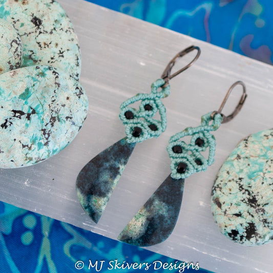 Teal macrame Bacan stone dangle earrings with black seed bead accents displayed beside pale textured stones