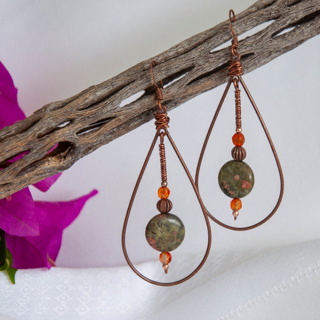 Wire wrapped copper teardrop earrings with unakite disc and carnelian beads, hanging from driftwood with bougainvillea