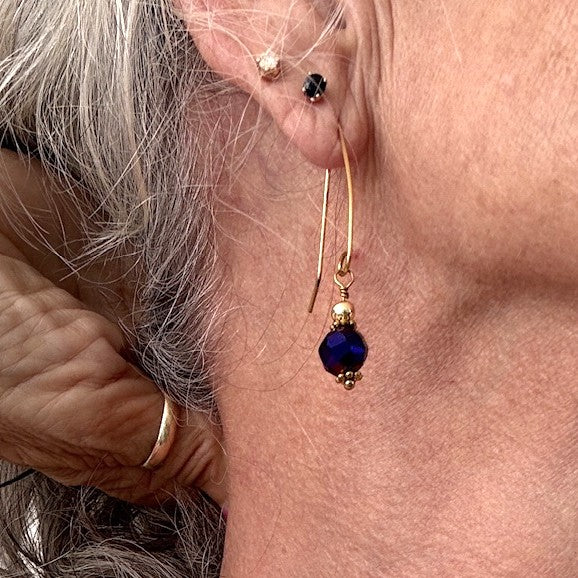 Cobalt blue vitrail glass drop earring shown worn, with an 8mm faceted glass bead and brass marquise hook wire.