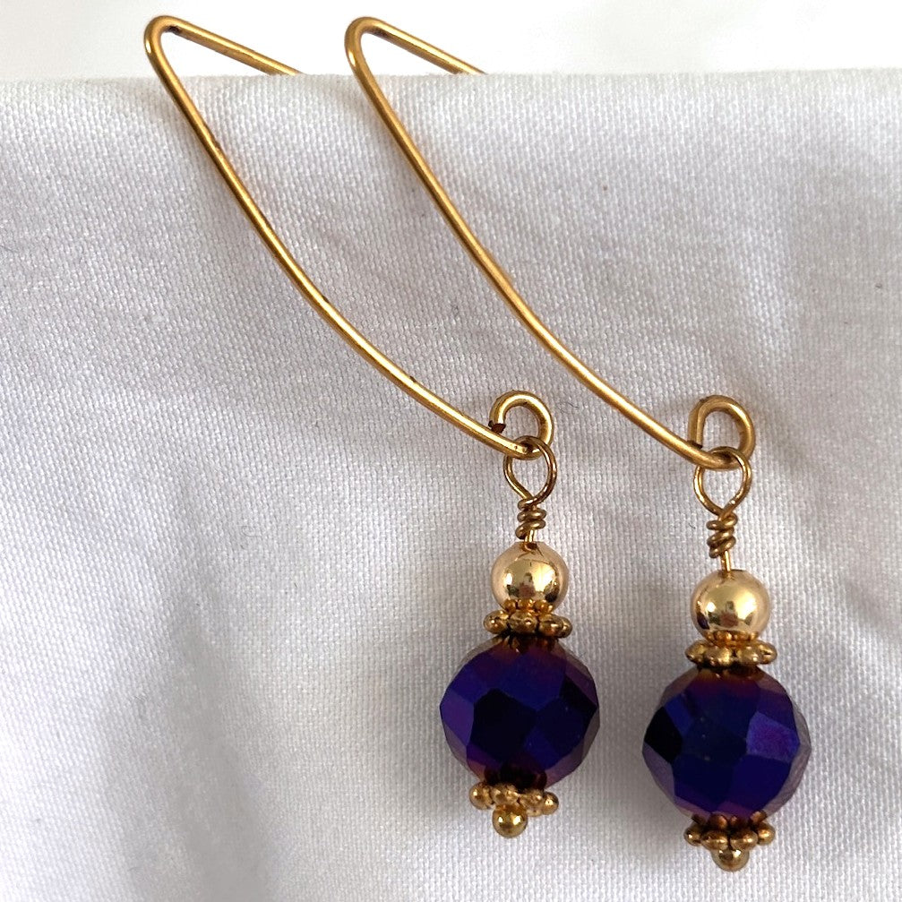 Cobalt blue vitrail glass drop earrings with 8mm faceted glass beads, gold-tone daisy spacers, and brass marquise hook wires on white.