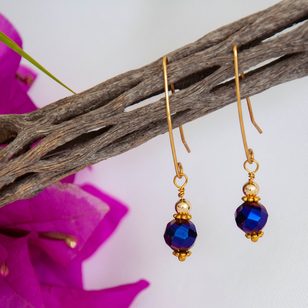 Cobalt blue vitrail glass drop earrings hanging from driftwood with magenta bougainvillea.