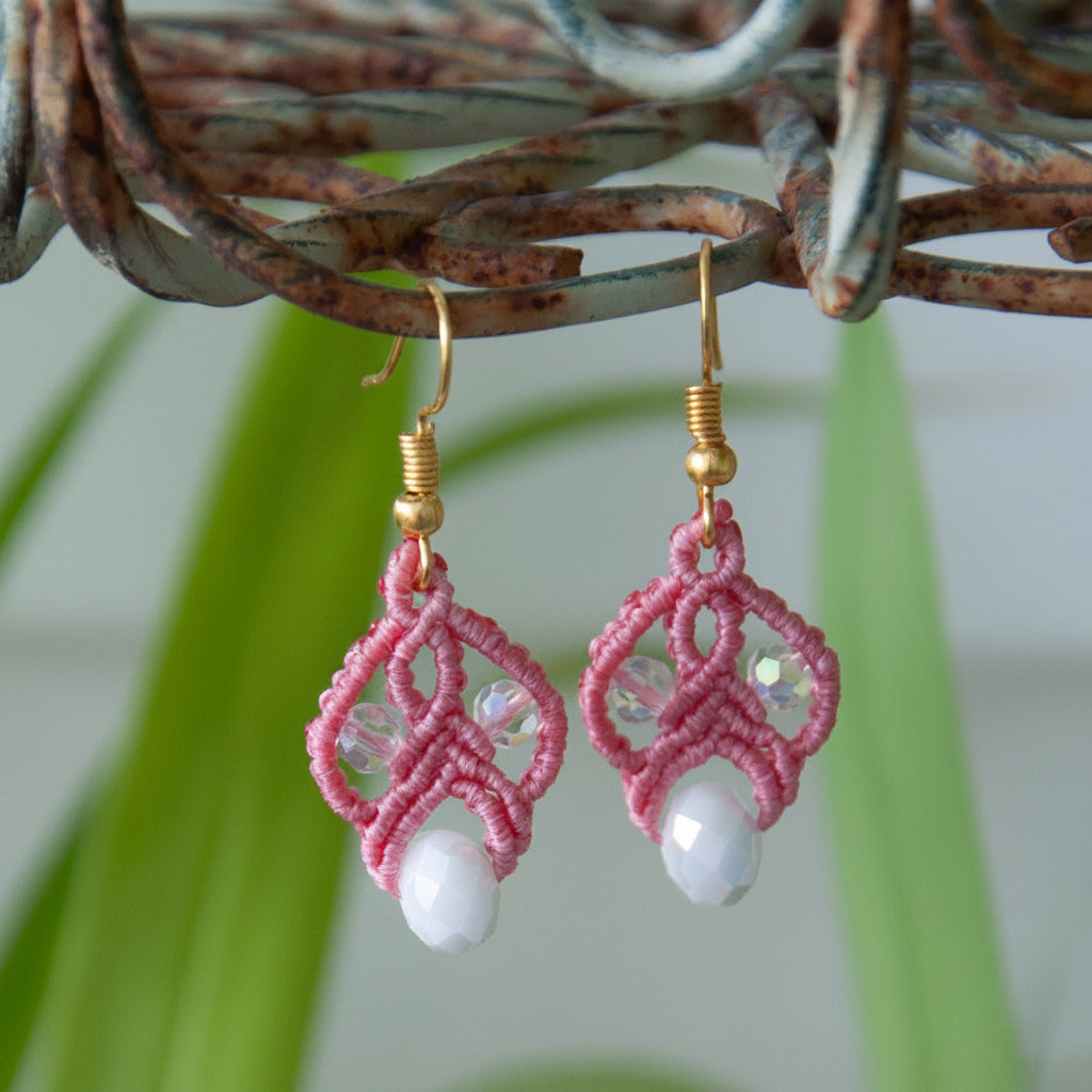Salmon pink macrame lace earrings with iridescent crystals and white rondelle drops on a leafy branch.