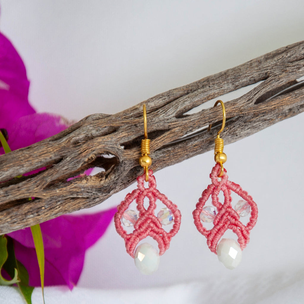 Salmon pink macrame lace earrings with iridescent crystal beads and white rondelle drops, styled on driftwood.