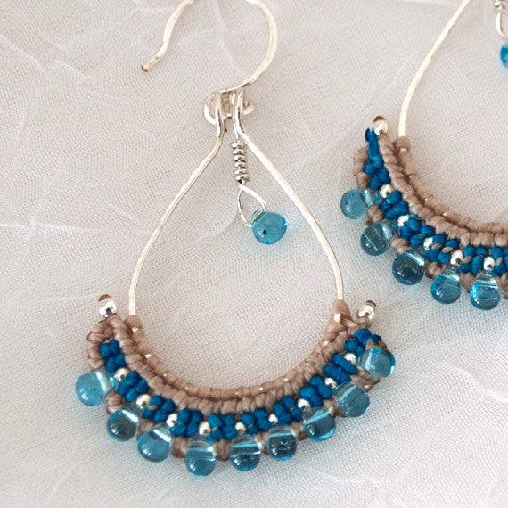 Close-up detail of hammered silver teardrop hoop earring showing teal and beige macrame knotwork, light blue Miyuki teardrop bead fringe, and wire-wrapped teardrop charm