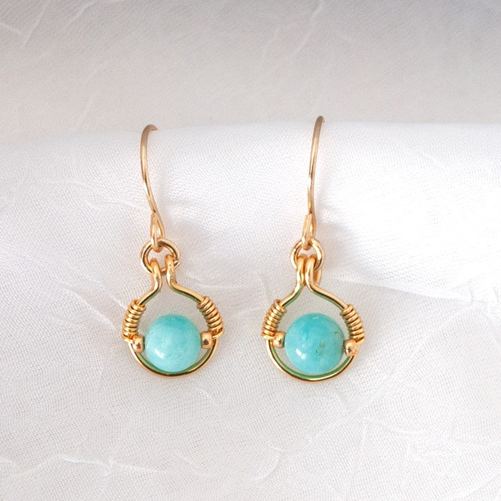 Handmade amazonite earrings with 6mm round amazonite bead in brass wire halo with galvanized gold seed bead accents and handcrafted brass ear wires, displayed on white linen background