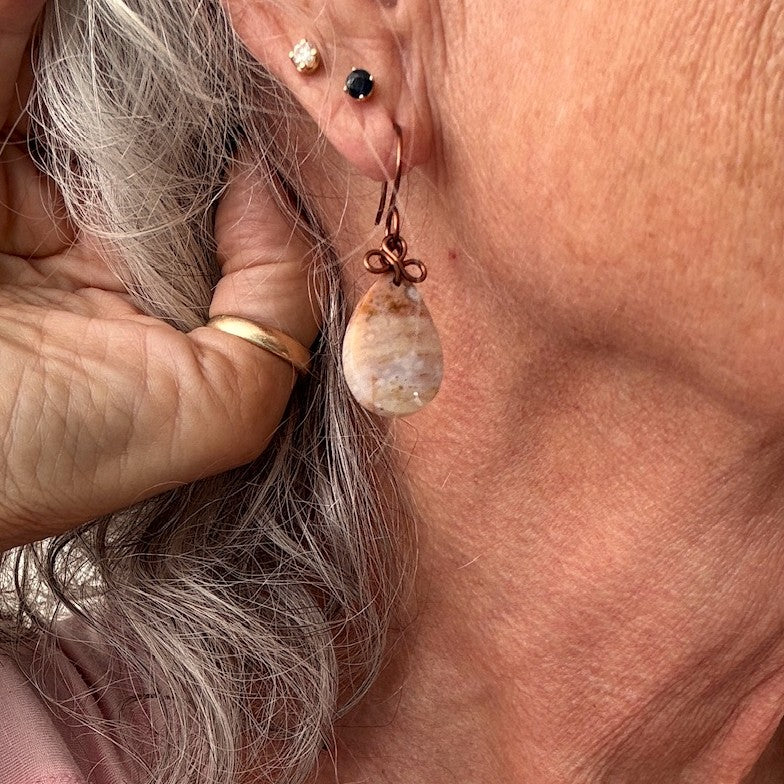 Handmade ocean jasper cabochon drop earring with antique copper wire bow worn in ear, showing scale and wearability — one-of-a-kind artisan boho gemstone earring by MJ Skivers Designs.