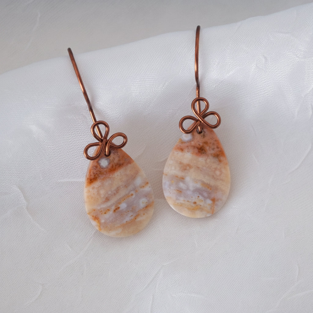 Handmade ocean jasper cabochon drop earrings with 15x26mm smooth teardrop ocean jasper, handcrafted antique copper wire bow, and handcrafted fishhook ear wires, laid on white linen fabric.