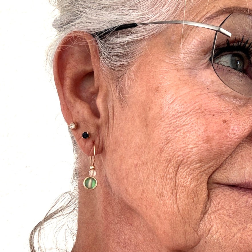 Close-up of a person wearing a green mermaid glass drop earring with a white faceted agate bead and handcrafted brass wire.