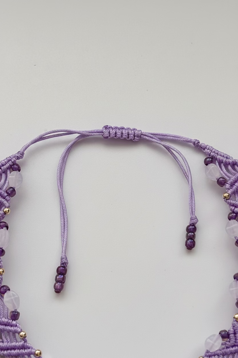A lavender macrame double zig zag anklet with purple seed beads, silver accent beads, and three gold flower charms, laid flat on a white background showing the full piece and slide closure.