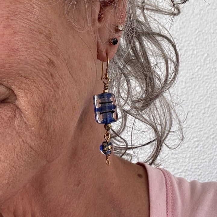 Handmade cobalt blue lampwork glass drop earring with 13mm × 15mm rectangular bead, black brushstroke detail, and 8mm coordinating round lampwork bead drop shown worn on model with silver hair.