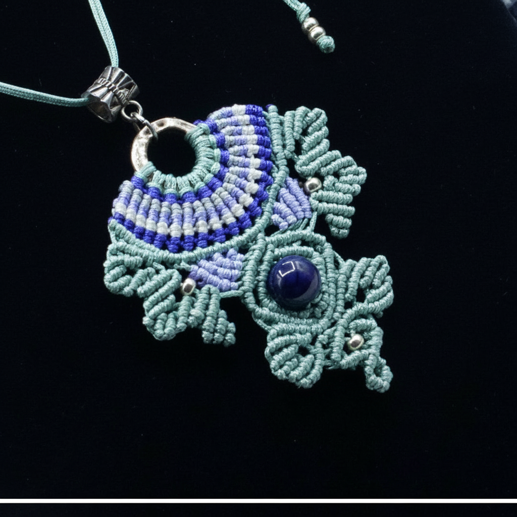 A handmade macrame pendant necklace featuring a circular ring, a dark and light purple and white patterned top section, and a lower section with light green and purple woven details, an Amethyst bead, and silver-toned metal accents, displayed on a black background.