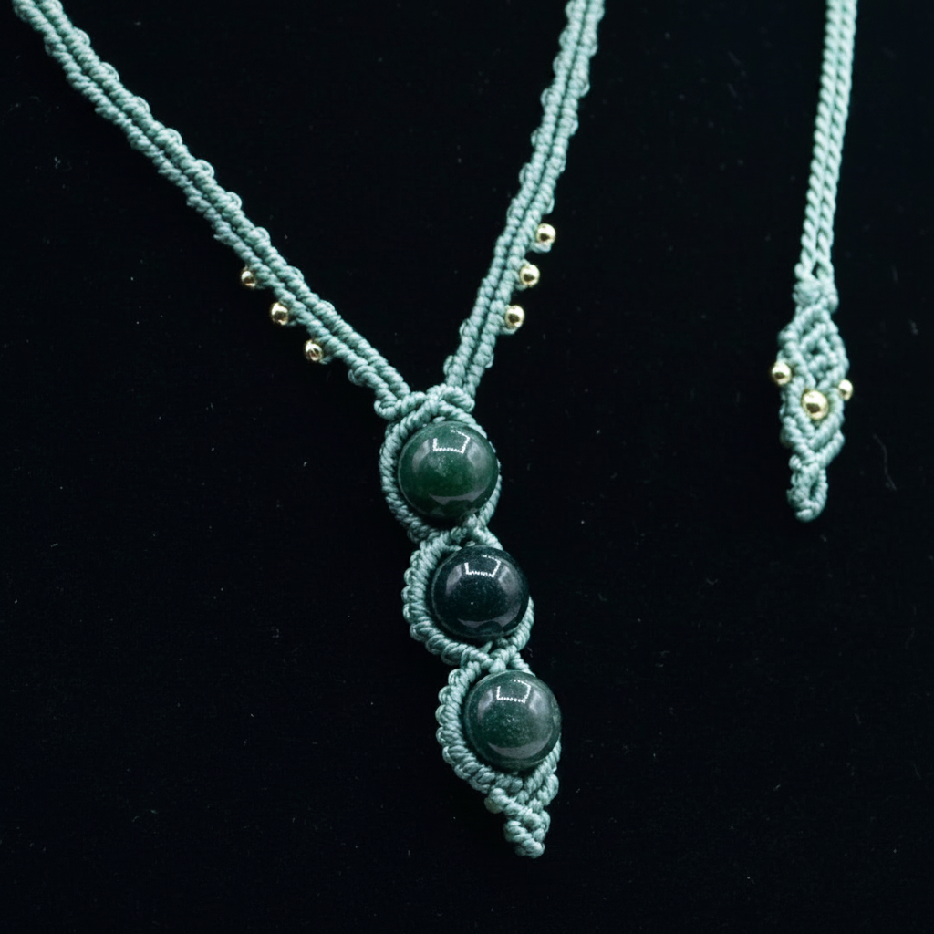 A handmade macrame necklace with three dark green polished beads, displayed on a black background. A matching macrame cord end is partially visible on the right side.