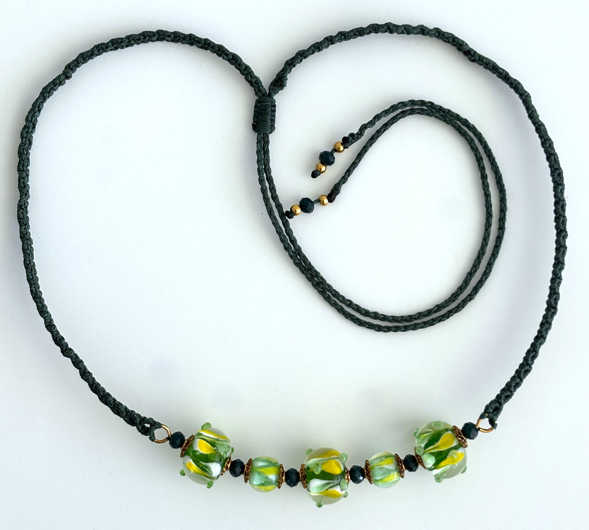 Clear lampwork glass macrame necklace with yellow, green, and white swirls, dark green cord, and adjustable slide closure.