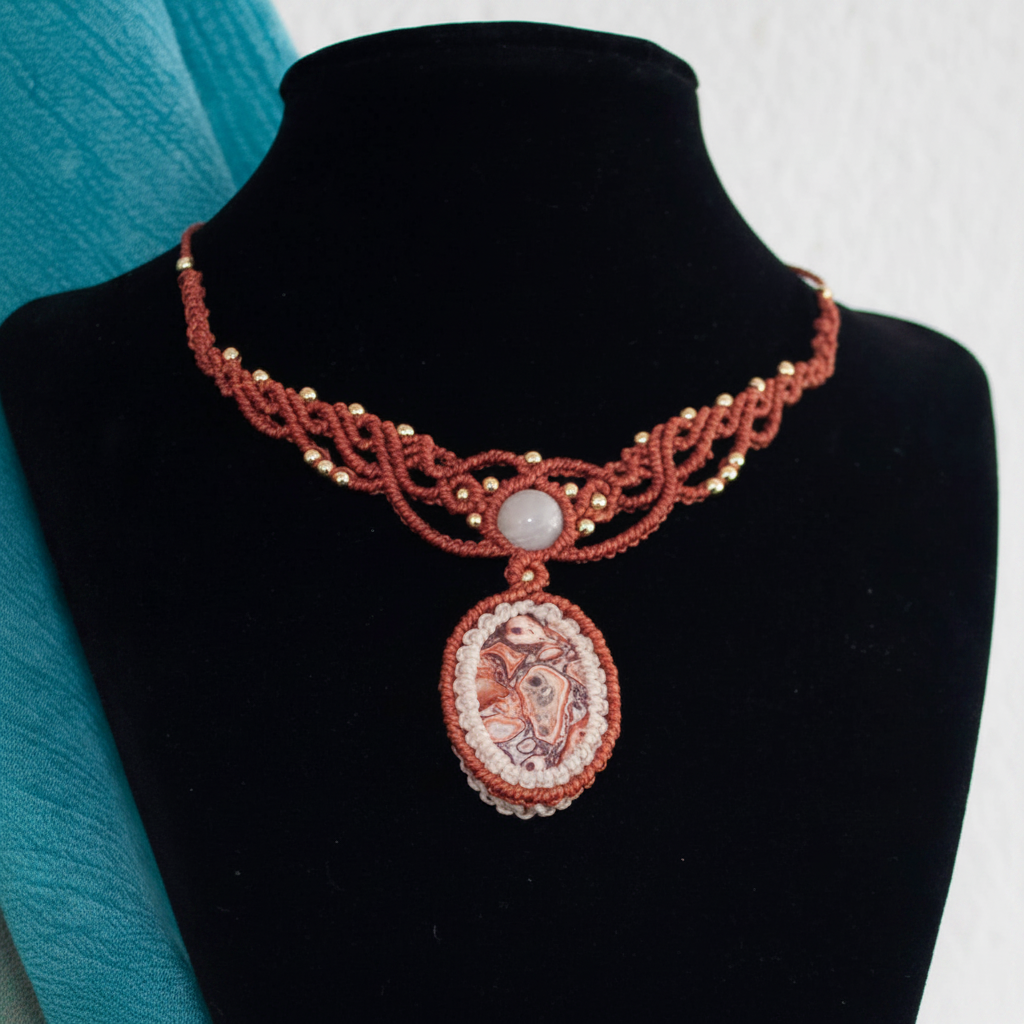 A handmade terracotta red and white braided cord necklace with a central oval pendant, displayed on a black velvet jewelry bust.