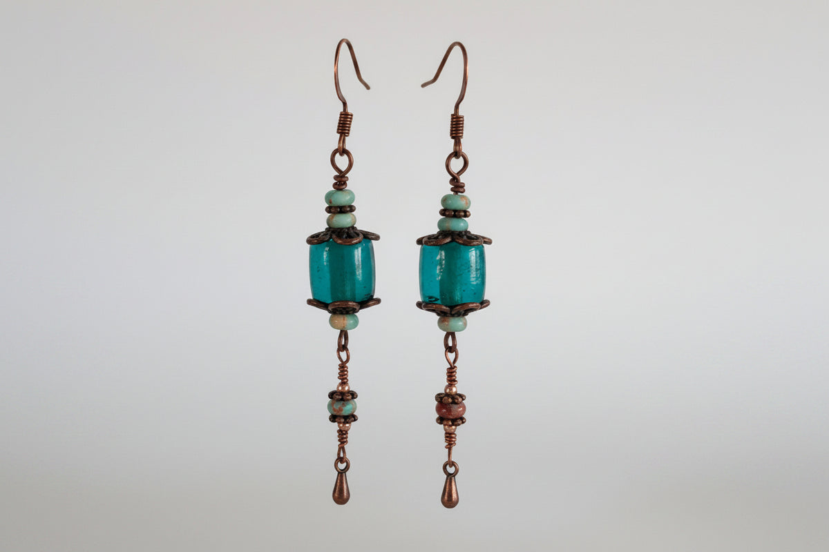Handmade teal dyed glass drop earrings with copper filigree caps, abacus-shaped blue sea sediment beads, daisy spacers, and wire-wrapped copper waterdrop charm — one-of-a-kind boho gemstone earrings.