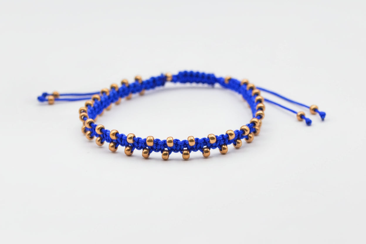 A royal blue macrame bracelet with galvanized gold seed beads on a clean white background.