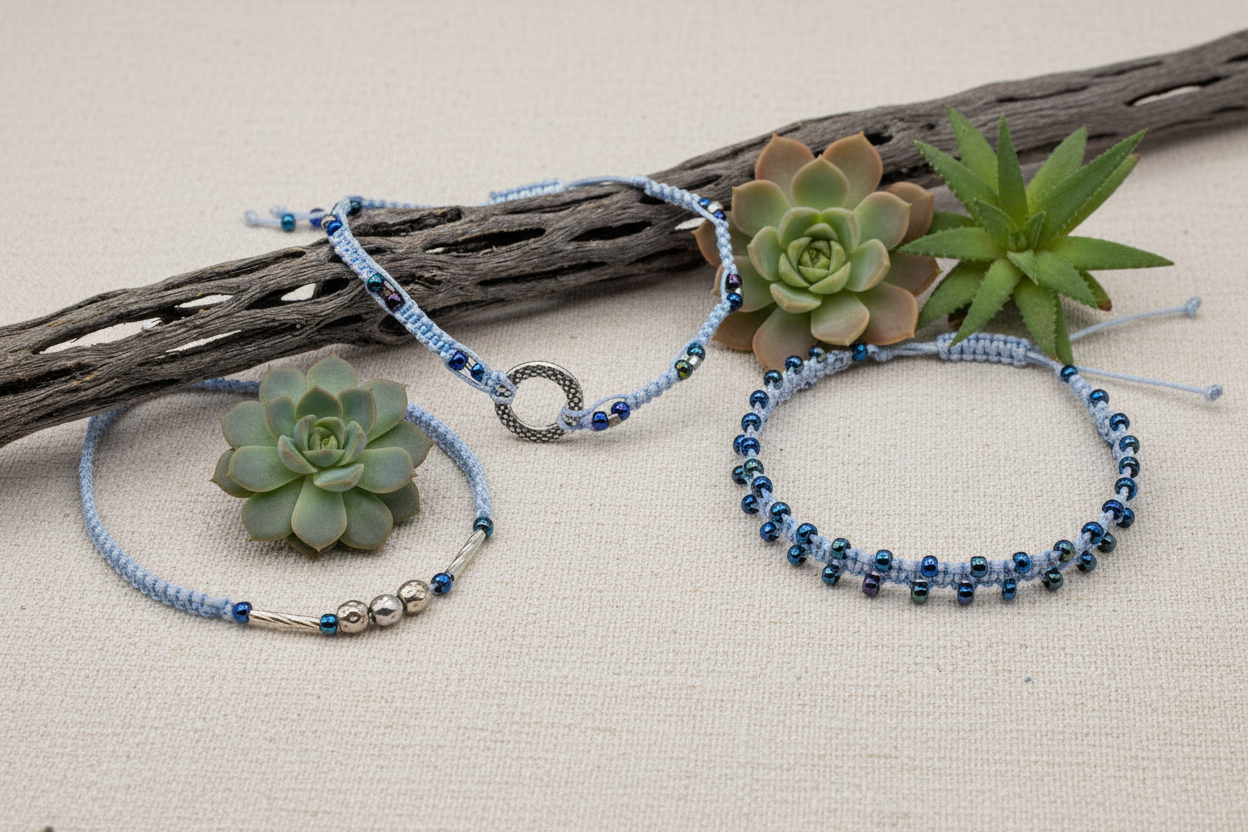 Three light blue macrame bracelets laid flat on linen fabric with driftwood and succulents, showcasing metallic blue seed bead and silver accent bead designs