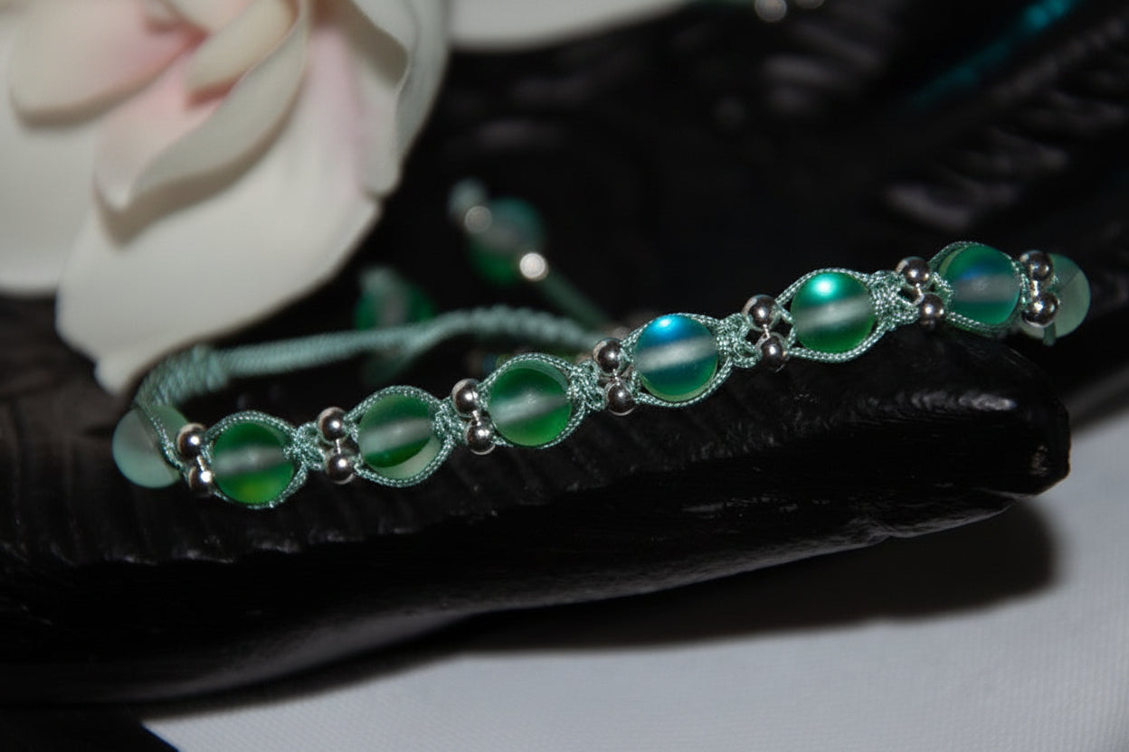A handmade beaded macrame bracelet with round frosted green glass beads and silver-toned metal bead accents, displayed on a black textured surface.