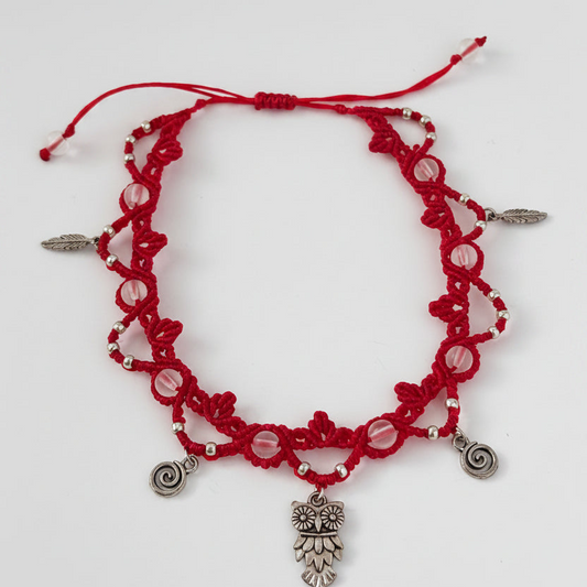 A red macrame beaded anklet with frosted clear mermaid glass beads, silver-toned charms, including an owl pendant, spiral charms, and small feather accents, displayed on a plain white background.
