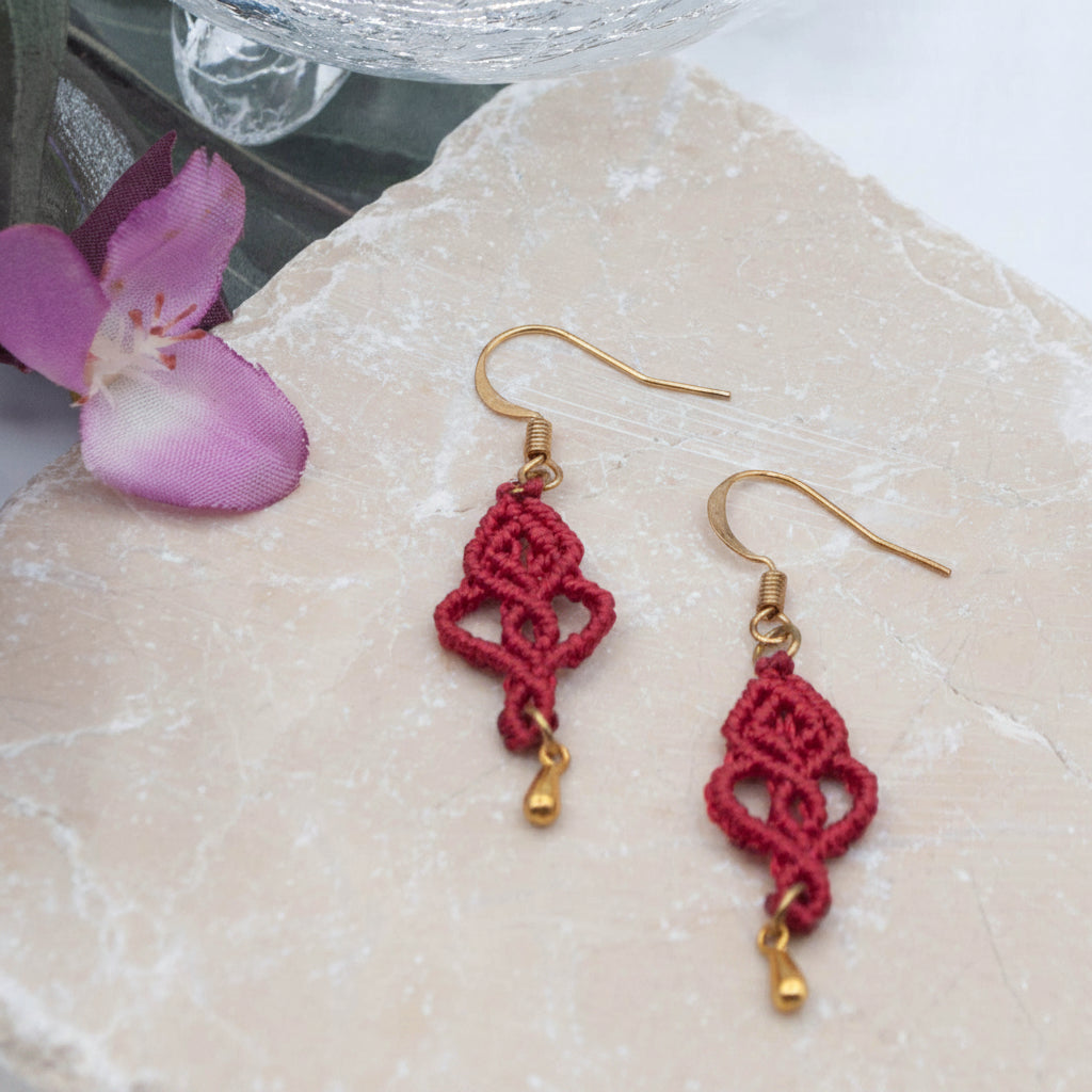 Handmade red macrame looping hearts earrings with gold-tone fish hook wires and teardrop charm on stone with pink flower — boho jewelry by MJ Skivers Designs.