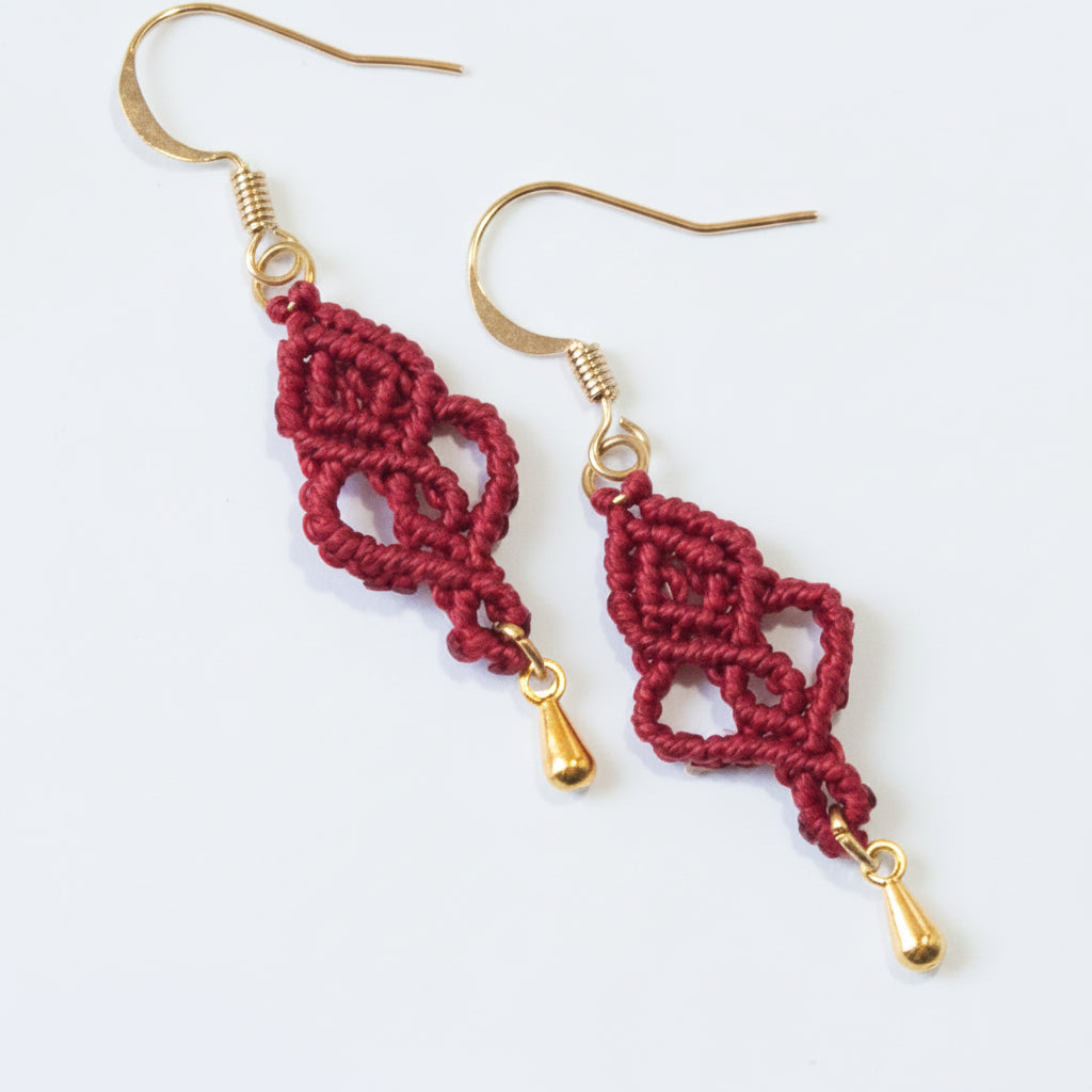 Handmade red macrame looping hearts dangle earrings with gold-tone teardrop charms and gold-tone fish hook wires, displayed on a clean white background.