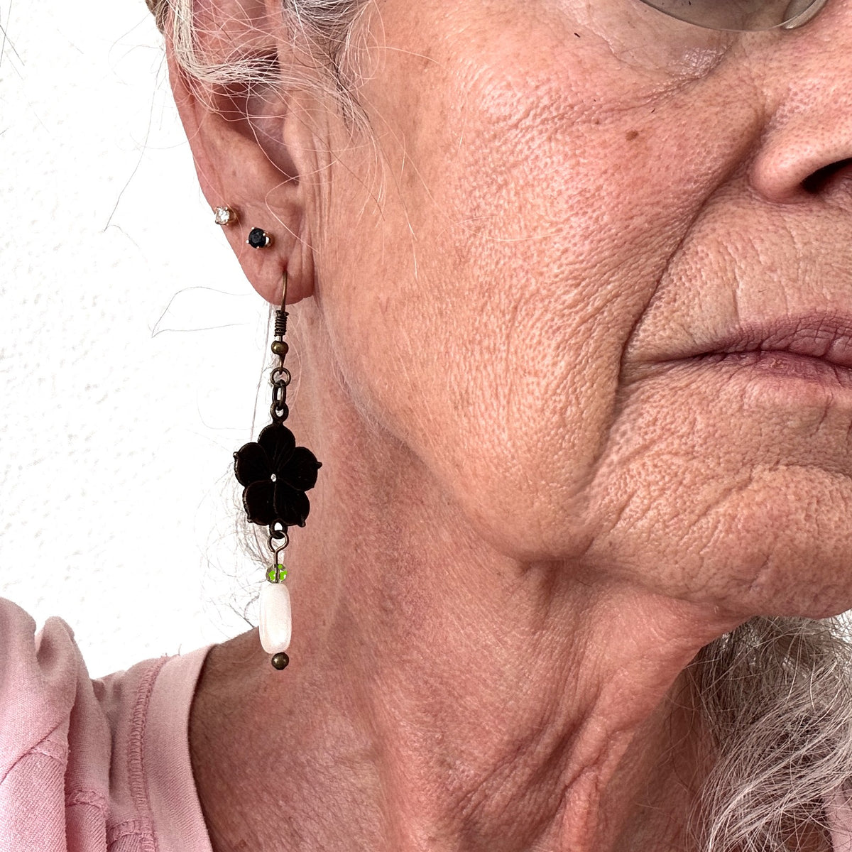 Bronze flower charm earring with mother of pearl drop and light green crystal bead shown worn on model with silver hair