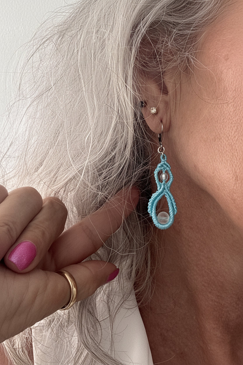 Close-up of a handmade turquoise macrame double drop earring with an iridescent mermaid glass bead worn on a model's ear with silver-tone lever-back closure.