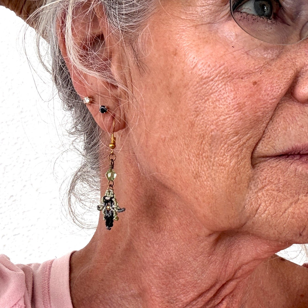Macrame earring in light green, black, and silver gray with wire-wrapped bicone bead shown worn on model with silver hair