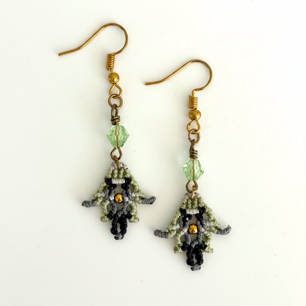 Handmade macrame earrings in light green, black, and silver gray with wire-wrapped light green bicone bead and gold-tone accent, displayed on white background