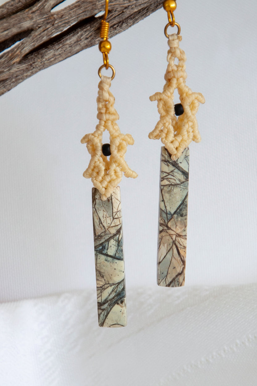 Pale yellow lace macrame pagoda earrings with maligano jasper stick bead, hanging from driftwood against a soft neutral background
