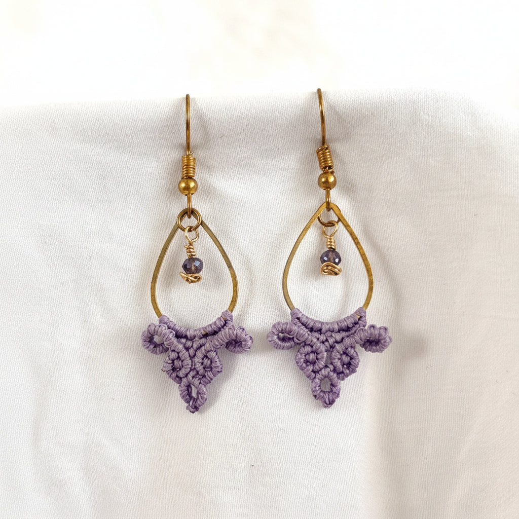 Pair of handmade lavender macrame fan drop earrings with gold-tone teardrop hoops and brass wire-wrapped faceted purple crystal beads, displayed on white fabric background.