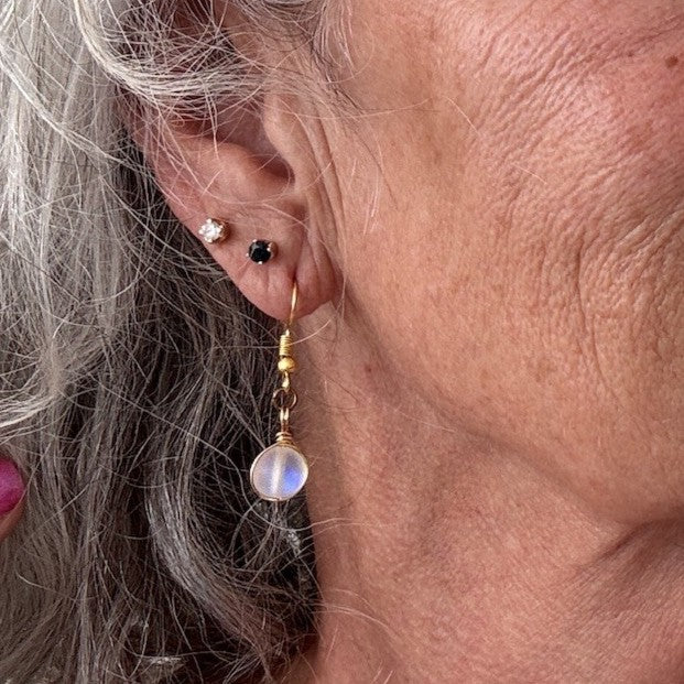 Handmade frosted mermaid glass drop earring with brass wire wrapping and gold-tone fish hook wire, shown worn on model with silver hair.
