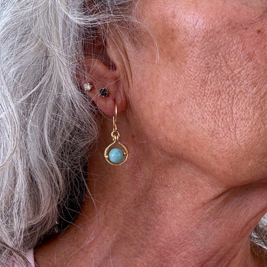 Amazonite earring with 6mm round amazonite bead in brass wire halo and gold seed bead accents shown worn on model with silver hair, close-up view showing construction detail