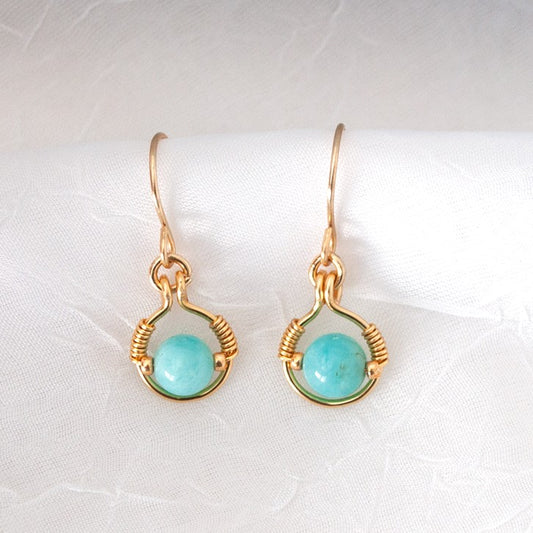Handmade amazonite earrings with 6mm round amazonite bead in brass wire halo with galvanized gold seed bead accents and handcrafted brass ear wires, displayed on white linen background