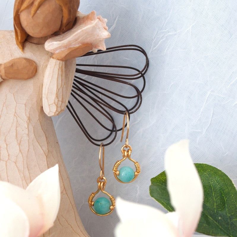 Handmade amazonite earrings with brass halo and gold seed bead accents displayed on Willow Tree angel figurine against blue-gray background with white magnolia