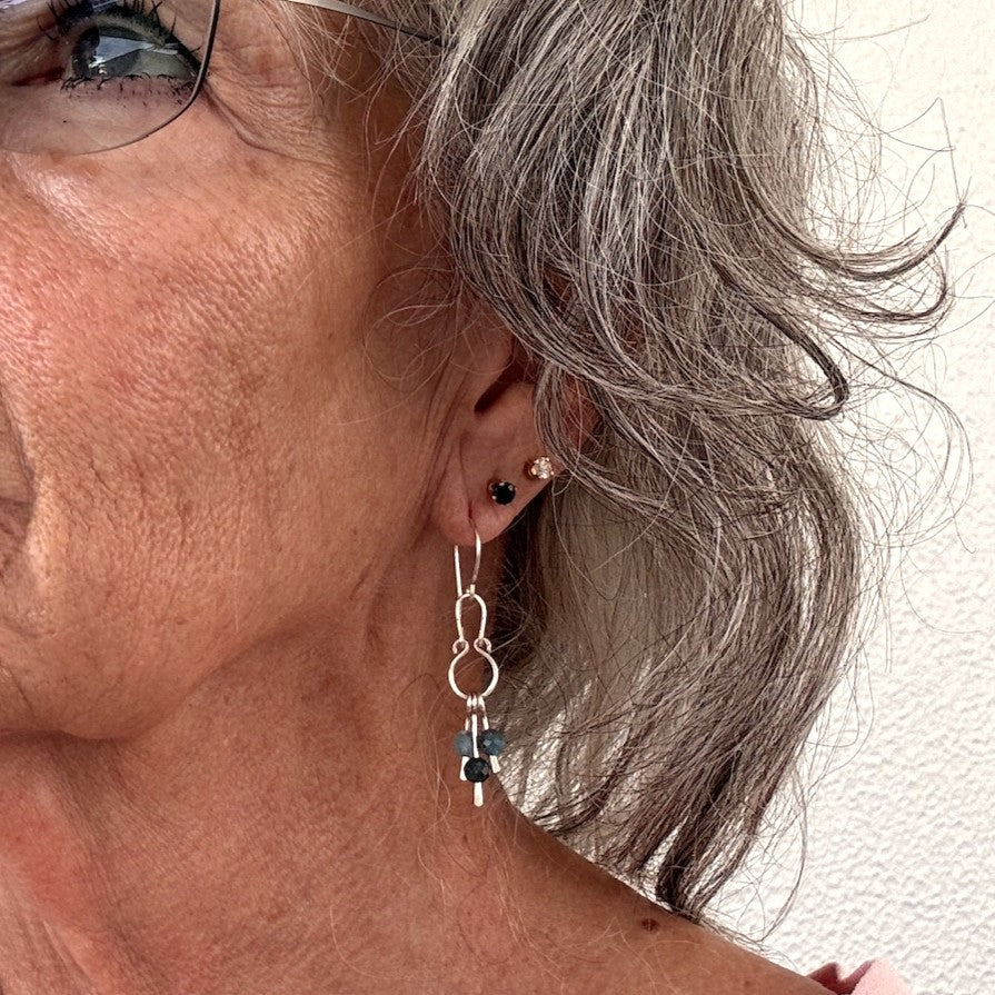 Apatite earrings with hammered silver chandelier frame and three faceted apatite bead dangles shown worn on model with silver hair and glasses