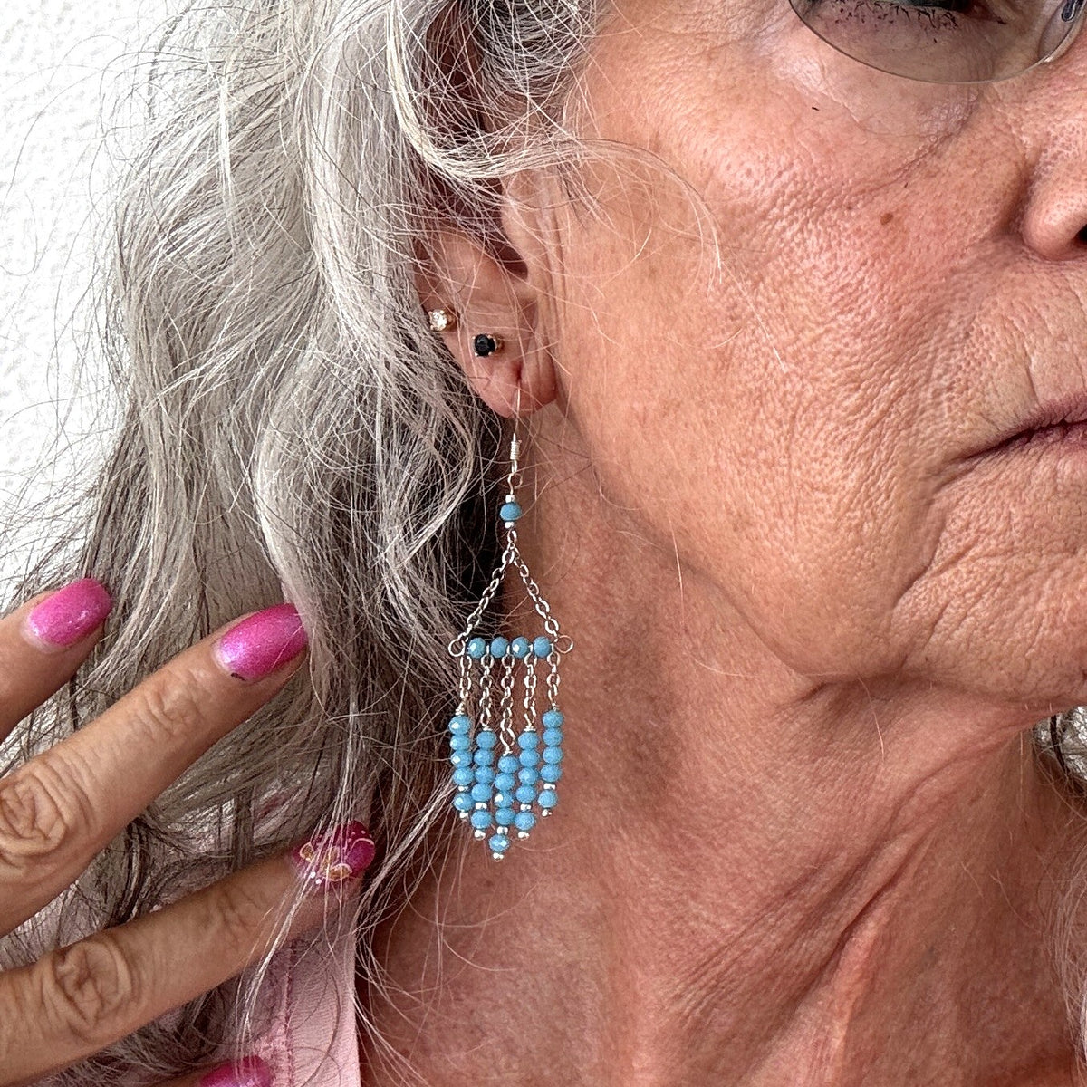 Turquoise color chandelier earring with five beaded strands and stainless steel chain frame shown worn on model with silver hair