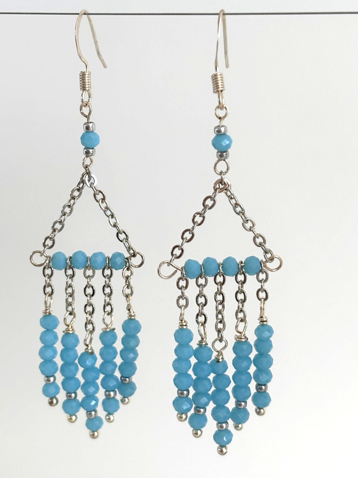 Handmade turquoise color chandelier earrings with five strands of faceted rondelle beads and stainless steel chain triangle frame, hanging against a white background